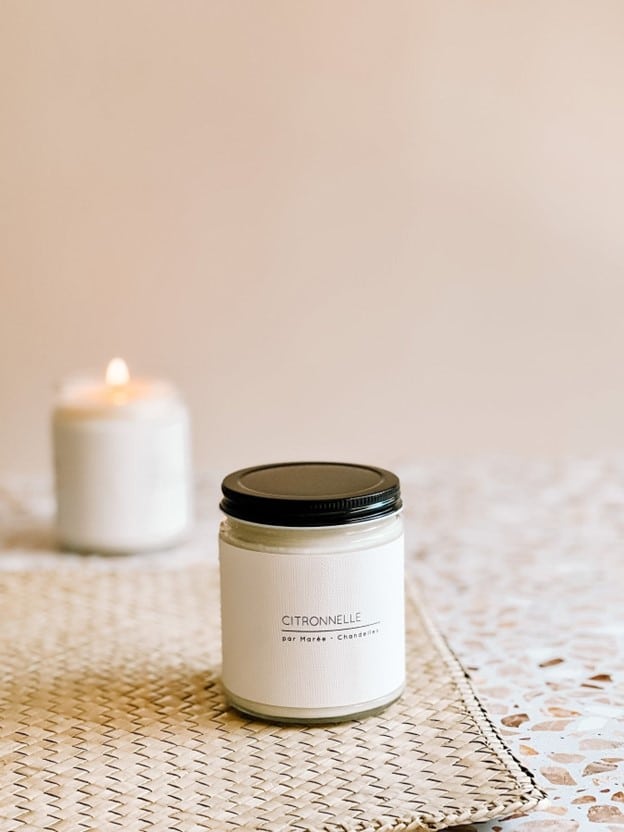 Chandelle de soya à la citronnelle allumée sur une table extérieure et une chandelle avec couvercle noir sur un napperon,diffusant une odeur fraîche et naturelle pour éloigner les moustiques.