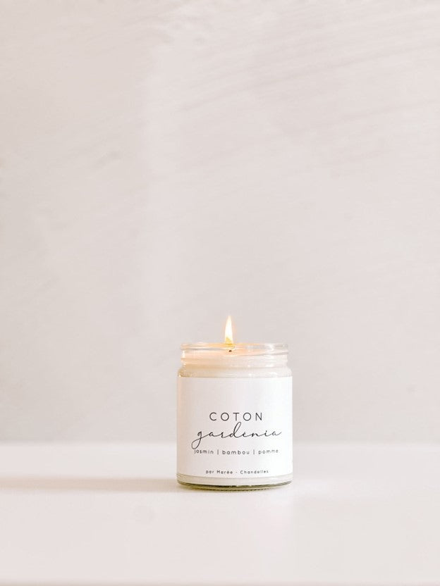 Chandelle de soya Coton Gardénia allumée dans un pot en verre , posée sur une surface lumineuse – flamme douce diffusant un parfum floral et frais de coton, gardénia et jasmin.