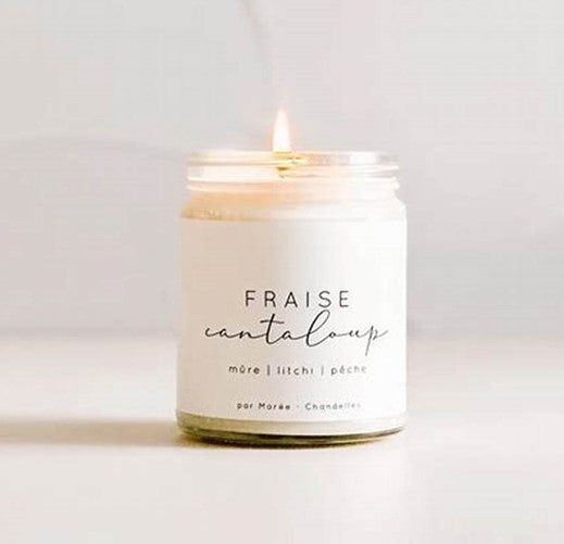 Chandelle de soya Fraise Cantaloup allumée dans un pot en verre , posée sur une surface blanche – flamme douce diffusant un parfum sucré et fruité, rappelant l’été et les fruits frais.