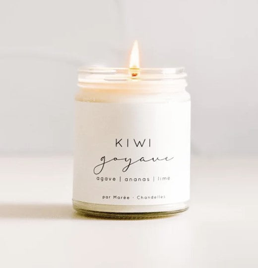 Chandelle de soya Kiwi Goyave allumée, dans un pot en verre avec couvercle blanc, posée sur une surface blanche – flamme douce diffusant un parfum tropical aux notes de kiwi, goyave, lime et ananas.