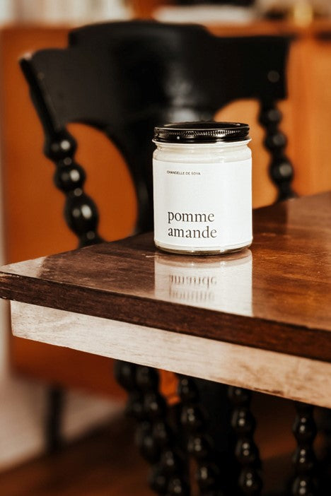 Chandelle de soya Pomme et Amande dans un pot en verre avec couvercle noir, non allumée, sur une surface en bois lustrée – chandelle artisanale au parfum fruité et doux, par Marée.