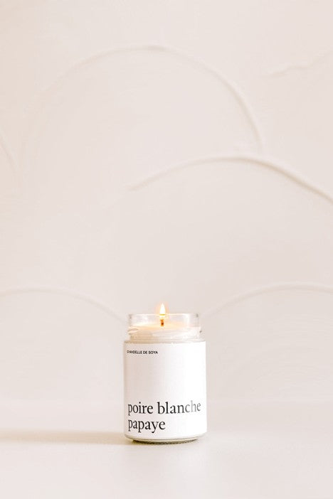 Chandelle de soya dans un pot de verre clair avec légère flamme, posée sur une table claire , dans une lumière naturelle douce.