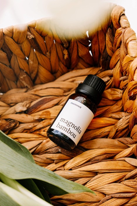 Bouteille de 15 ml de fragrance Magnolia bambou avec compte-goutte, posée dans un panier en osier ambiance florale et fraîche.