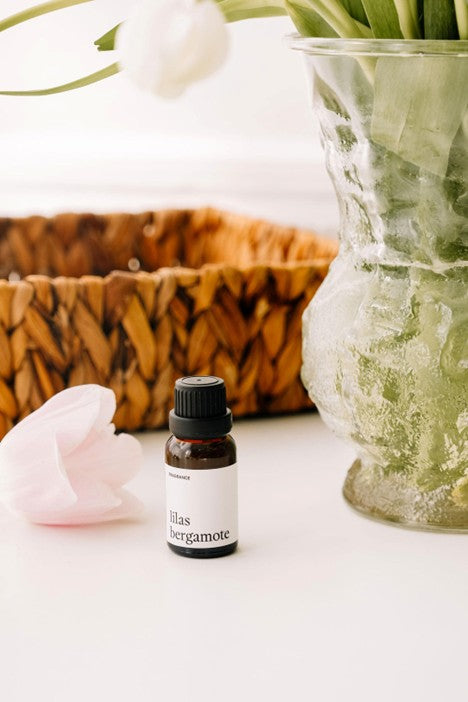 bouteille de fragrance lilas bergamote 15 ml pour balles de séchage déposé près d'un panier en osier et un pot à fleurs remplis de lilas blanc