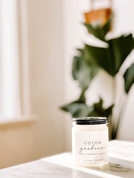 Chandelle de soya Coton Gardénia  dans un pot en verre avec couvercle noir, posée sur une surface lumineuse – flamme douce diffusant un parfum floral et frais de coton, gardénia et jasmin.
