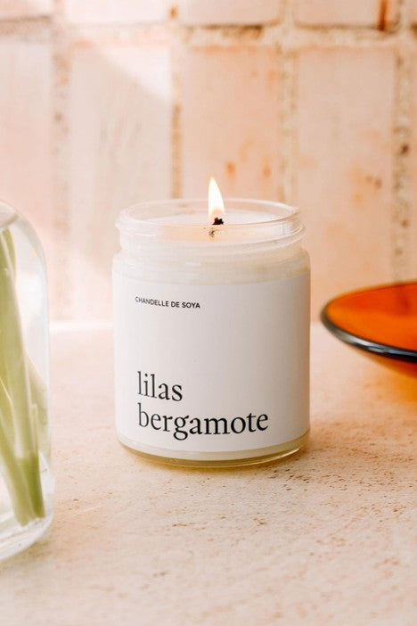 Chandelle de soya lilas et bergamote dans un pot en verre, posée sur une table en bois près d’un bouquet de fleurs printanières, diffusant un parfum doux et frais.
