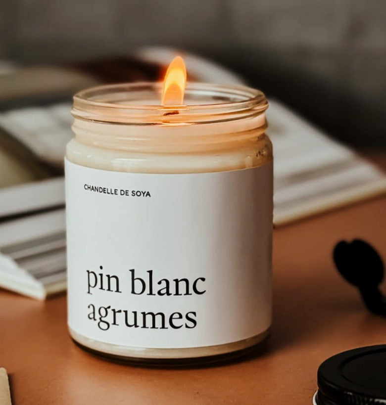 Chandelle de soya Pin Blanc & Agrumes allumée, dans un pot en verre , posée sur un comptoir rustique – flamme douce diffusant un parfum boisé et citronné rappelant la forêt après la pluie.

