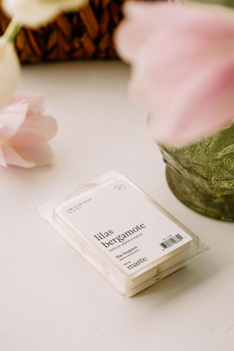  Cubes de cire de soya parfumés au lilas et à la bergamote présentés dans un emballage recyclable, avec 6 cubes parfumés d’un doux arôme floral et frais, posés à côté d’un diffuseur à cire.